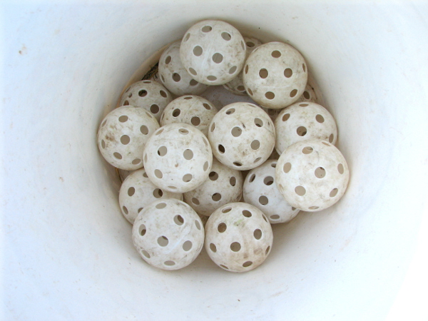 A bucket of plastic baseballs with holes, also known as wiffle balls